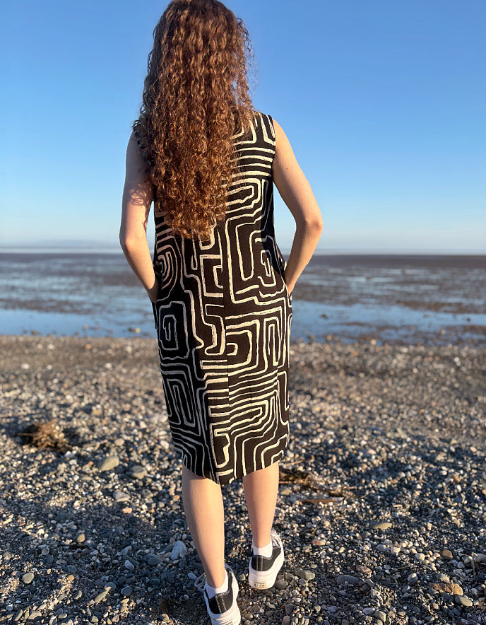 Person wearing a black and white patterned dress standing on a beach.