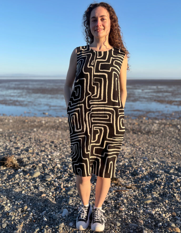 Person wearing a black and white patterned dress standing on a beach.