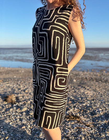 Person wearing a black and white patterned dress standing on a beach.