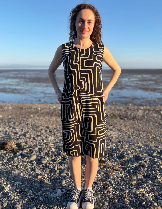 Person wearing a black and white patterned dress standing on a beach.