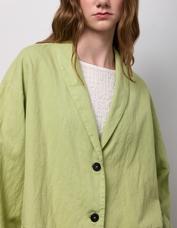 Person wearing a light green jacket over a white sweater on a plain background