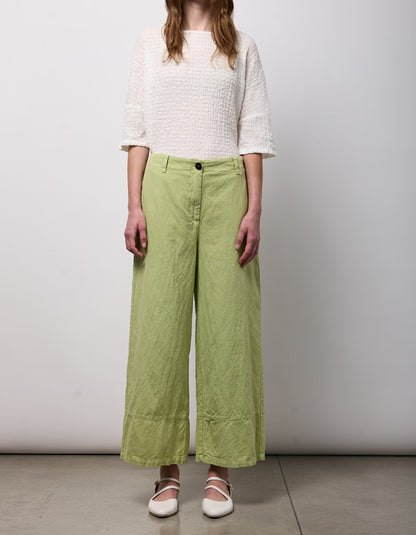 Person wearing a white textured top and green wide-leg pants on a plain background