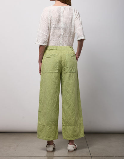 Person wearing a white top and green wide-leg pants against a plain background