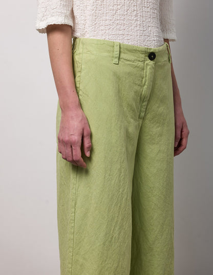 Person wearing light green pants and a white textured shirt on a plain background
