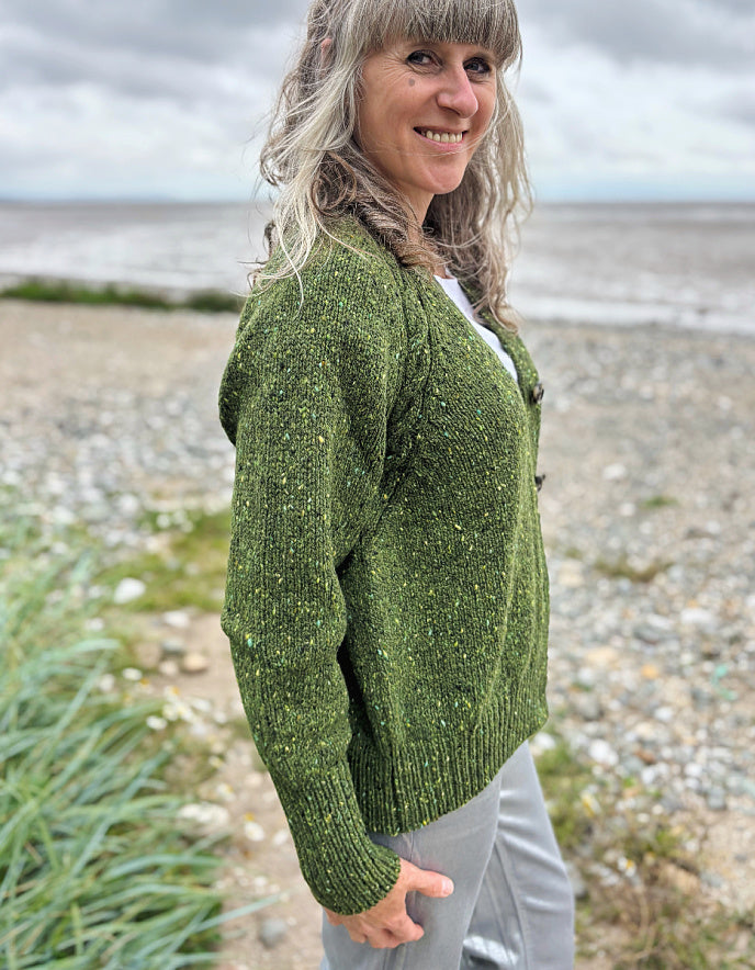 Woman wearing a green knitted cardigan standing on a beach.