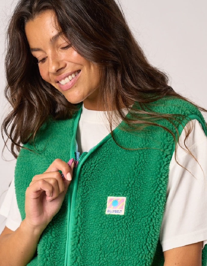 A woman wearing a bright green sherpa fleece zip-up vest over a white t-shirt, with the Allurbet brand logo visible on the chest.