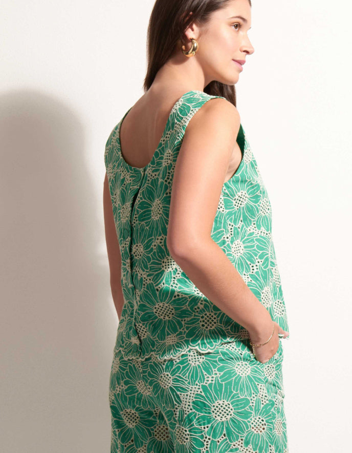 Woman wearing a green floral sleeveless top and pants on a plain background
