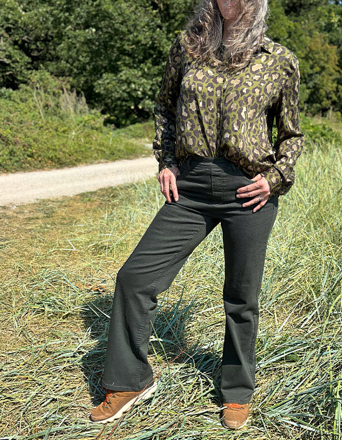 Person wearing a camouflage silk shirt and dark green pants standing on grass with trees in the background