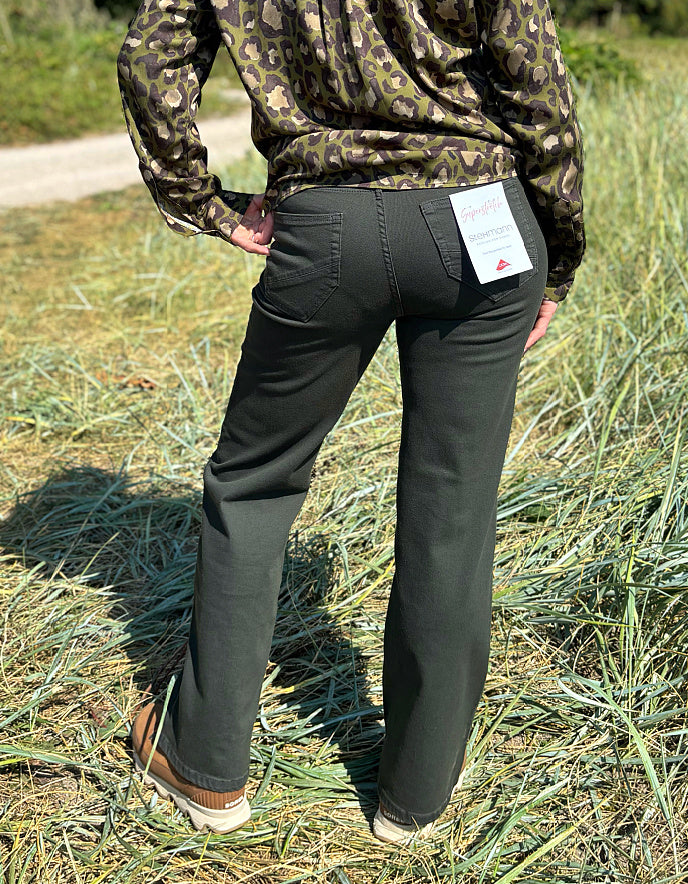 Person wearing camouflage jacket and green pants standing in a grassy field