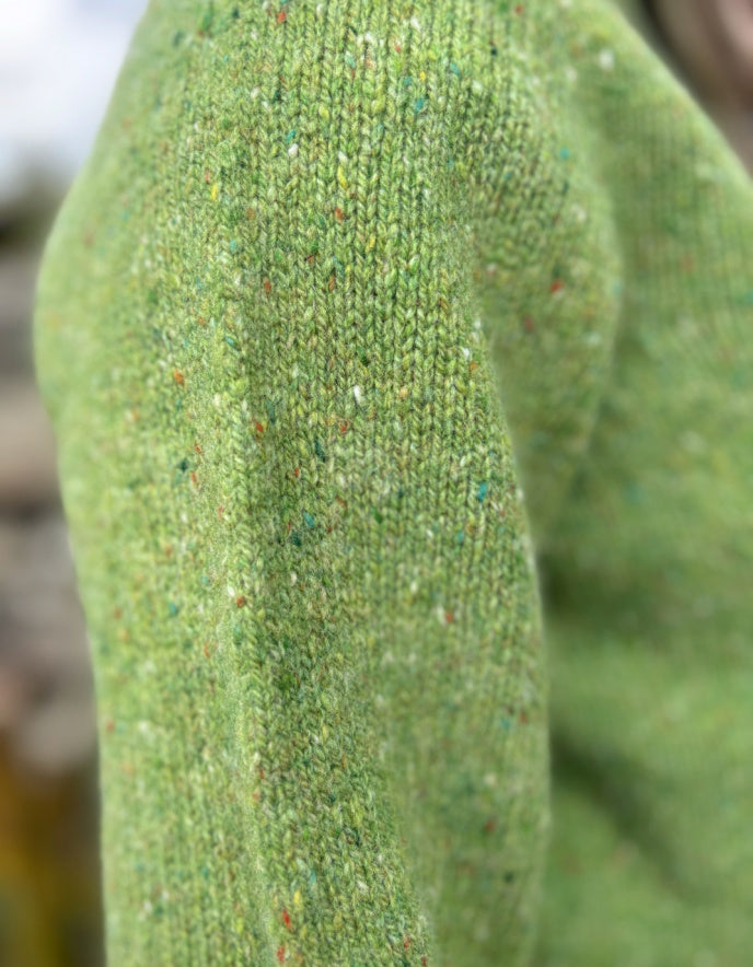 Close-up of a green knitted sweater sleeve with speckled pattern.