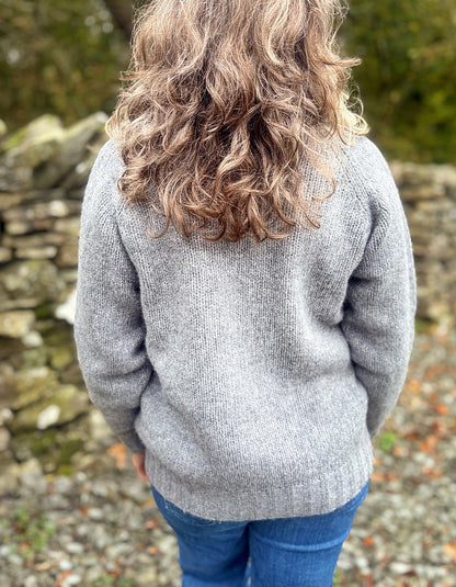 Person wearing a gray sweater with a blurred natural background