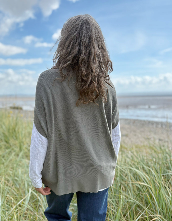 Woman wearing green slate grey tank top with relaxed fit over a white t shirt on a beach and blue sky in the background