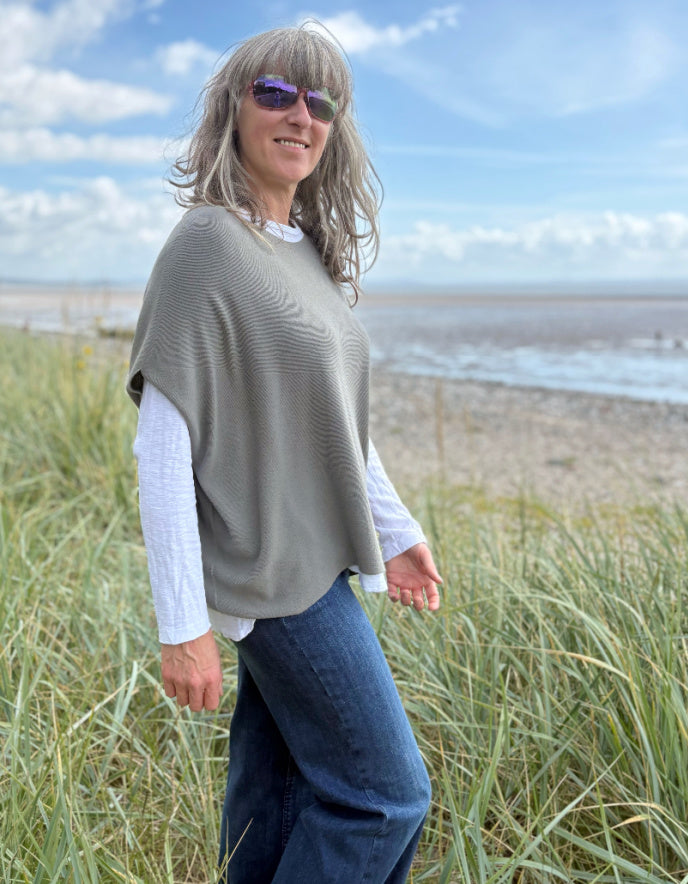 Woman wearing green slate grey tank top with relaxed fit over a white t shirt on a beach and blue sky in the background