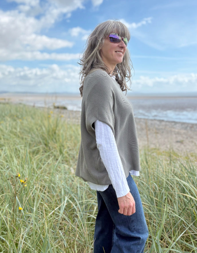 Woman wearing green slate grey tank top with relaxed fit over a white t shirt on a beach and blue sky in the background