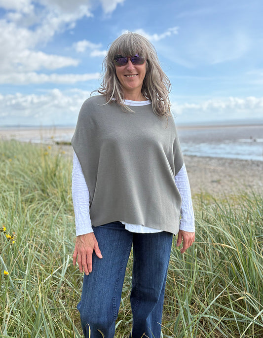 Woman wearing green slate grey tank top with relaxed fit over a white t shirt on a beach and blue sky in the background