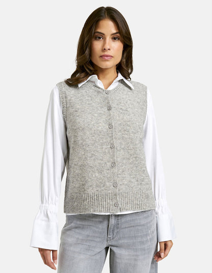 Woman wearing a gray sweater vest over a white shirt on a light gray background