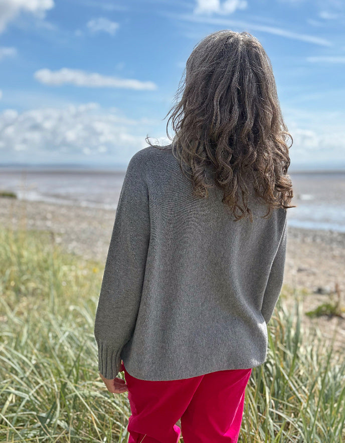 Person wearing a grey turtle neck sweater and sunglasses standing in a grassy field with a blue sky.