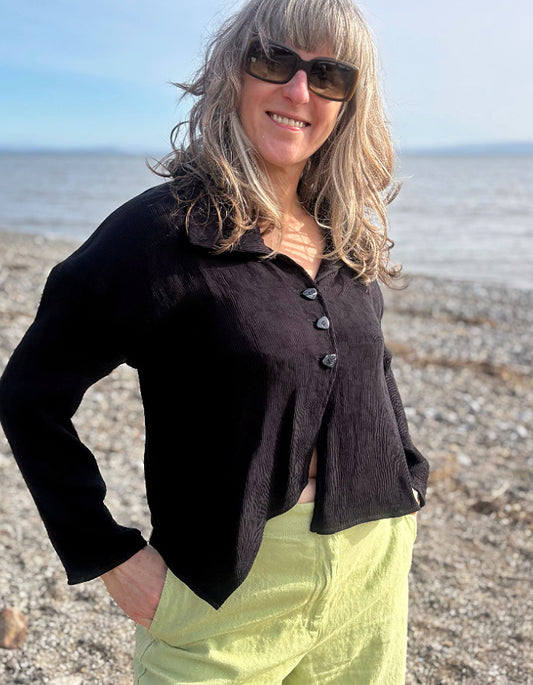 Woman wearing a black cropped jacket and sunglasses on a beach