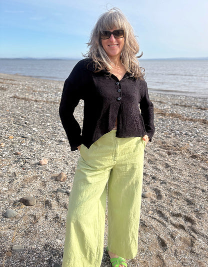 Woman standing on a beach wearing a black cardigan and bright green pants.