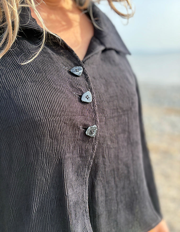 Close-up of a person wearing a dark gray button-up shirt with a blurred background