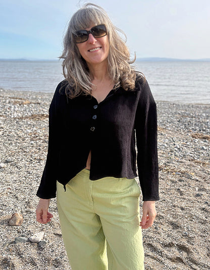 Woman standing on a beach wearing sunglasses, a black top, and light green pants.