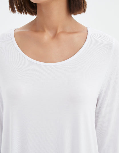 Close-up of a person wearing a white long-sleeve top with a plain background