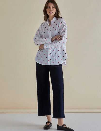 Woman wearing a white blouse with red patterns and black pants against a beige background