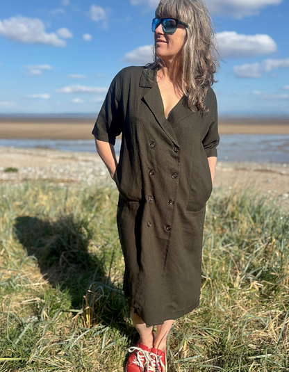 Woman in a green dress standing in a grassy field with a coastal background