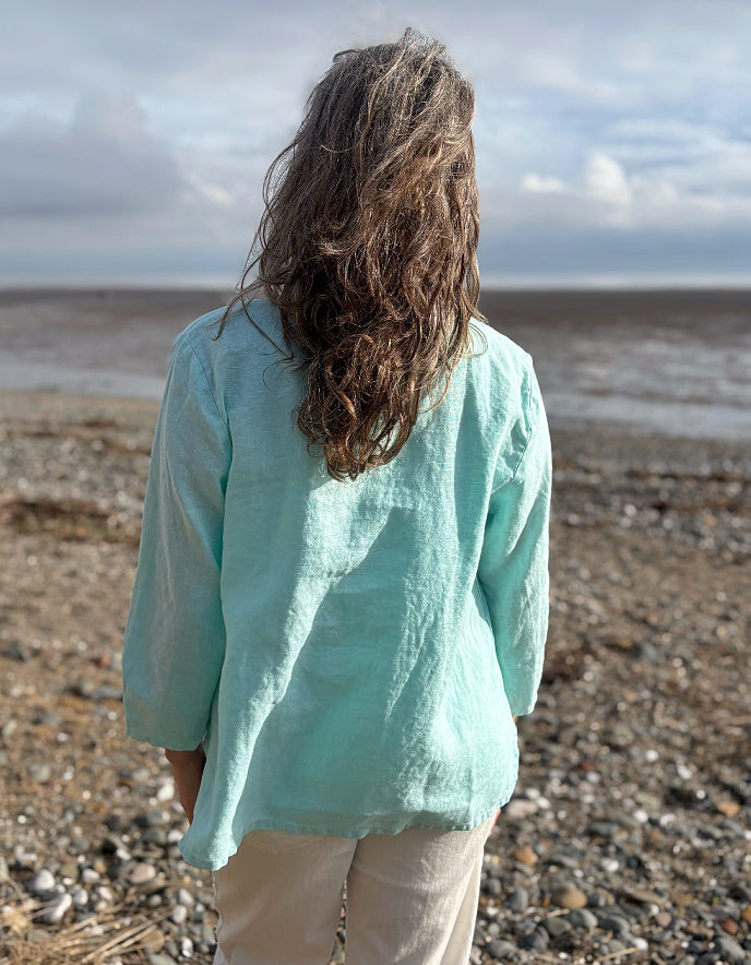 Person wearing a light blue shirt standing on a pebbly beach with a cloudy sky.