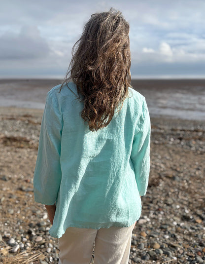 Person wearing a light blue shirt standing on a pebbly beach with a cloudy sky.