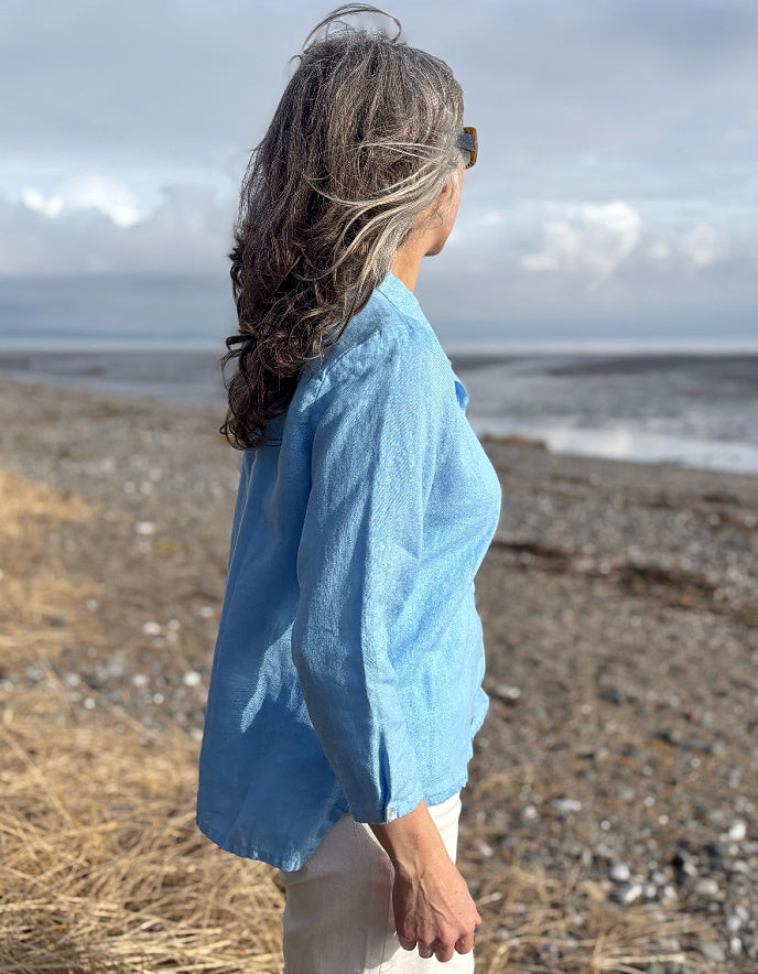 Person wearing a light blue shirt standing on a beach with a cloudy sky.