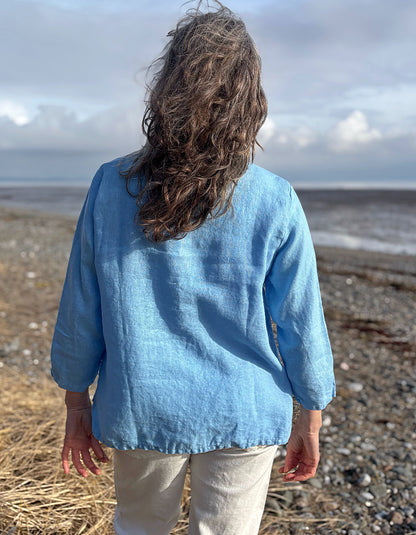 Person wearing a blue shirt standing on a beach with a cloudy sky.