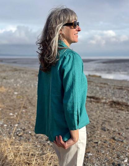 Person wearing a teal jacket standing on a beach with ocean and sky in the background