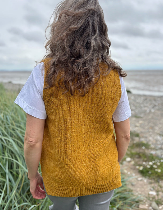 Person wearing a mustard yellow knitted vest on a beach
