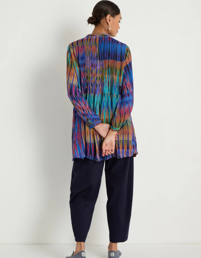 Person wearing a colorful patterned top and dark pants on a white background