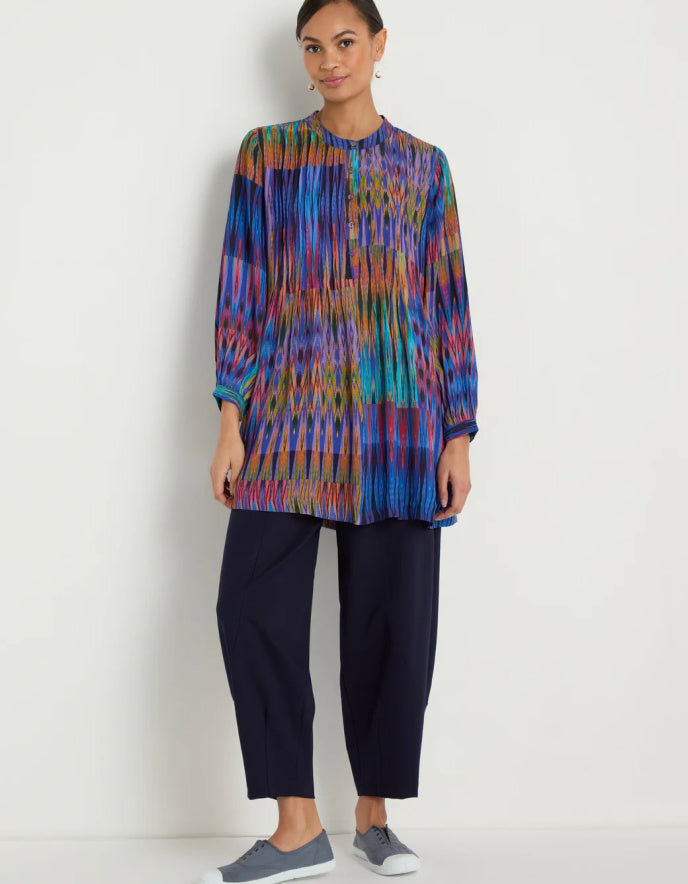 Woman wearing a colorful patterned top and dark pants on a white background