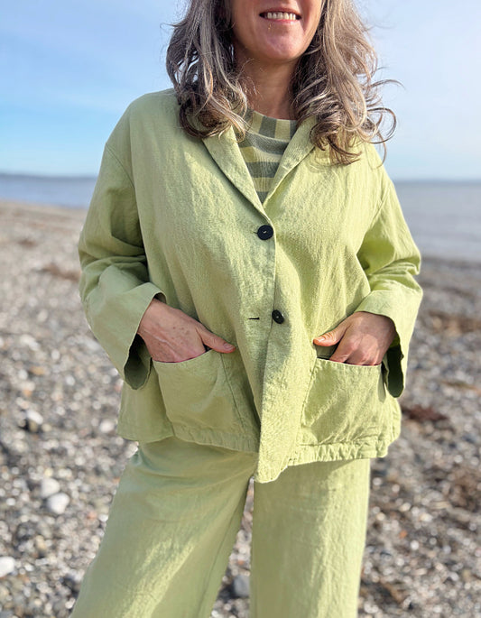 Person wearing a light green cotton linen suit standing on a pebbly beach.
