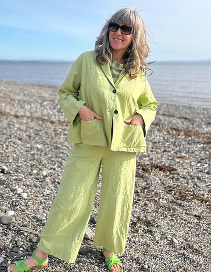 Person wearing a light green cotton linen suit standing on a pebbly beach.