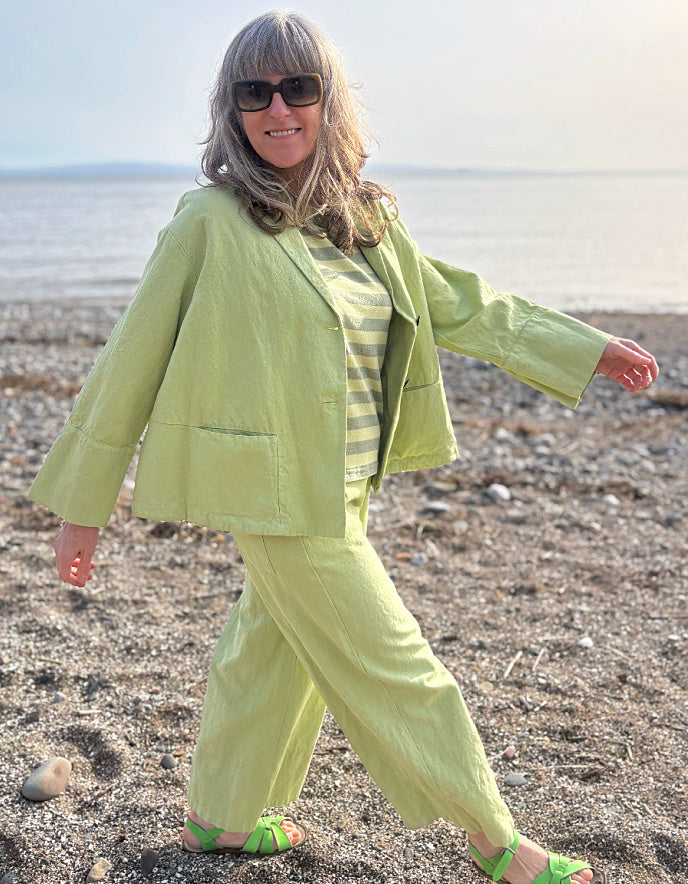 Person wearing a light green cotton linen pant suit standing on a pebbly beach.