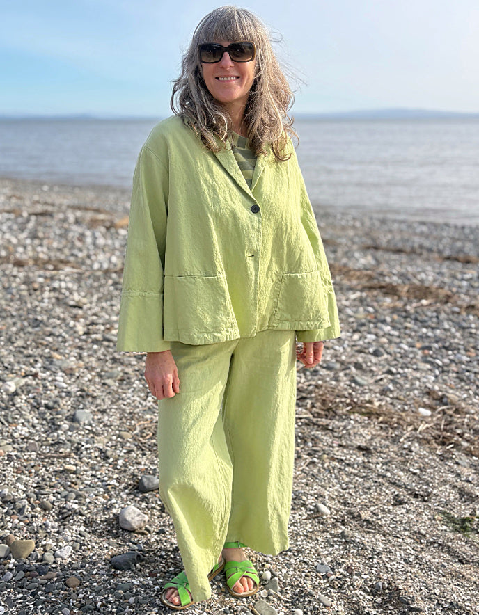 Person wearing a light green cotton linen pant suit standing on a pebbly beach.