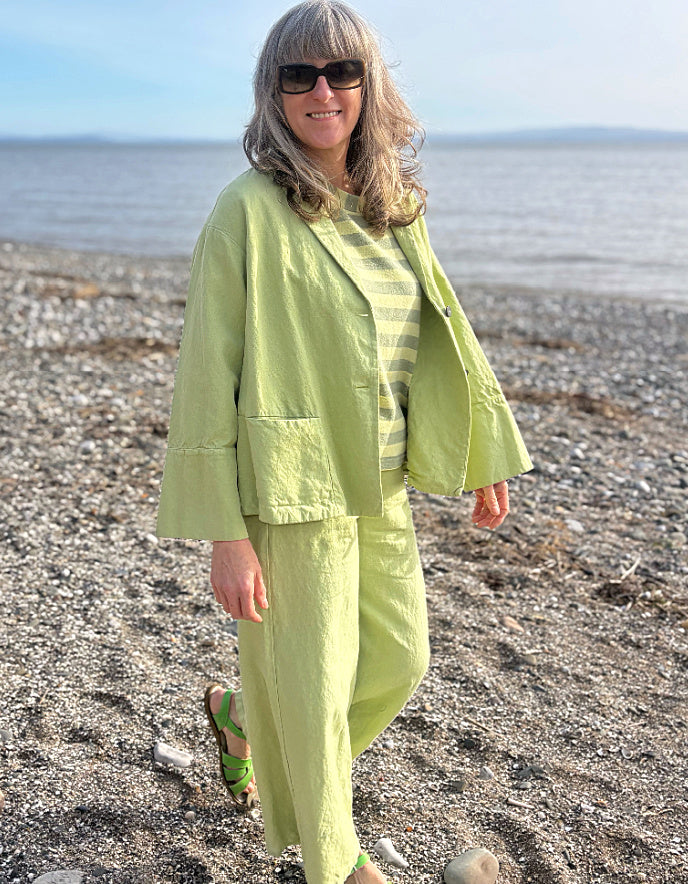 Person wearing a light green cotton linen pant suit standing on a pebbly beach.