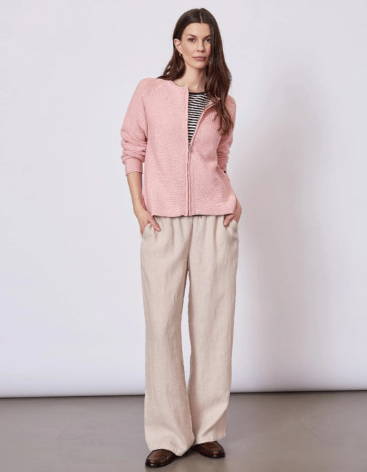 Woman wearing a pink cardigan and beige pants against a white background