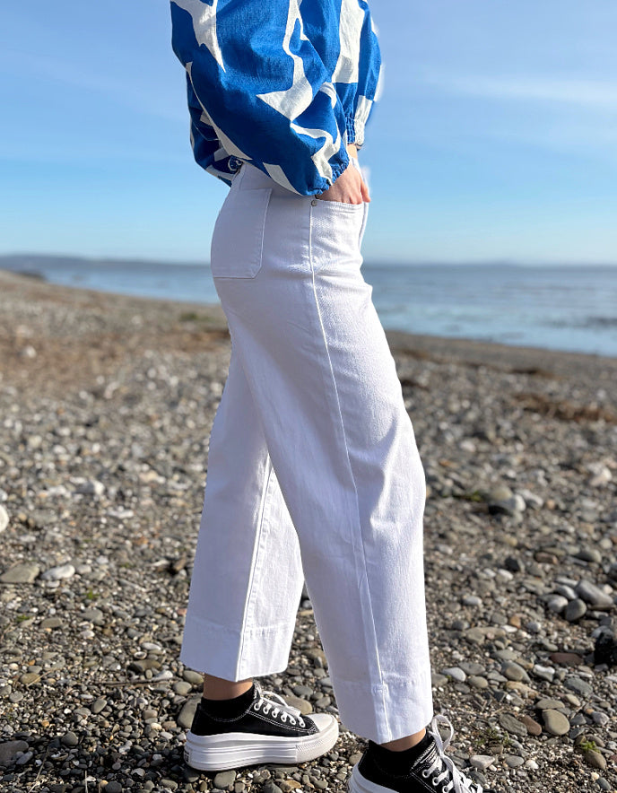 Person wearing a blue and white jacket, white pants, and black sneakers on a beach.