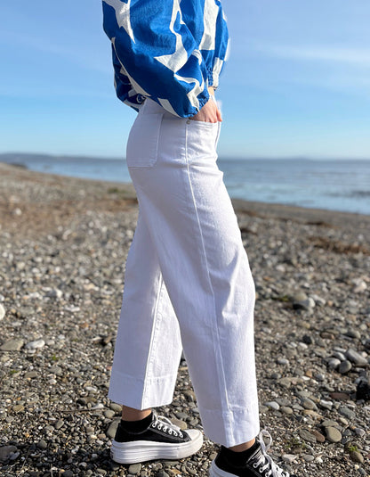 Person wearing a blue and white jacket, white pants, and black sneakers on a beach.