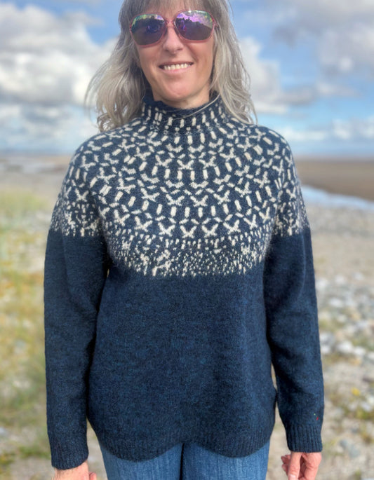 Person wearing a patterned navy sweater on a beach with a blue sky.