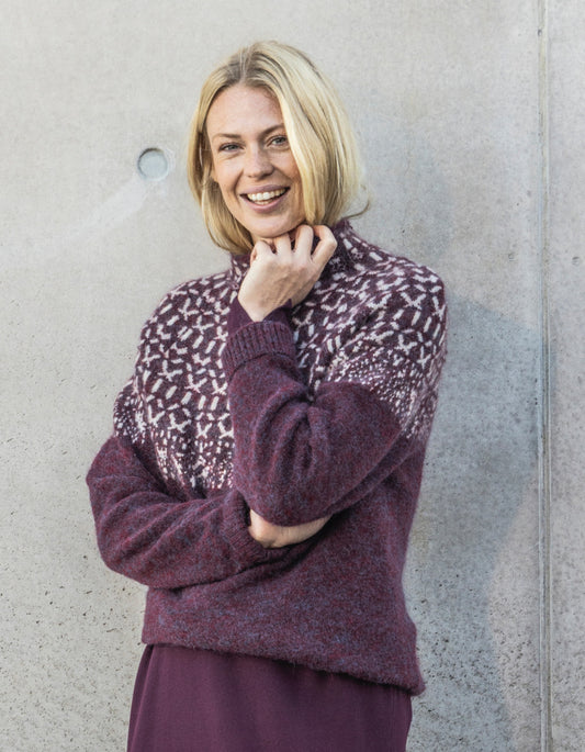 Woman wearing a patterned sweater against a plain wall