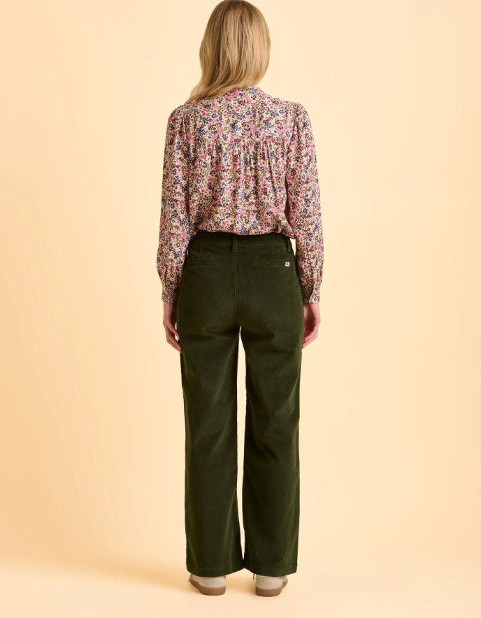 Person wearing a floral blouse and green pants on a beige background