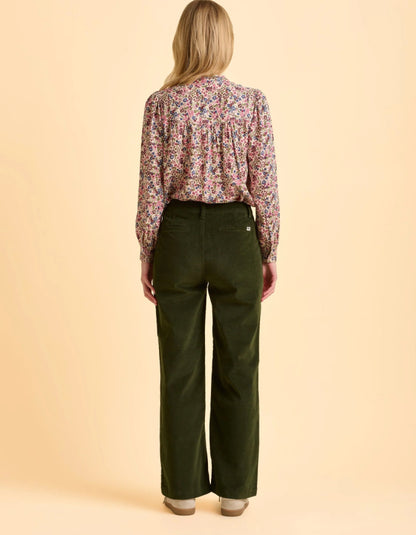 Person wearing a floral blouse and green pants on a beige background