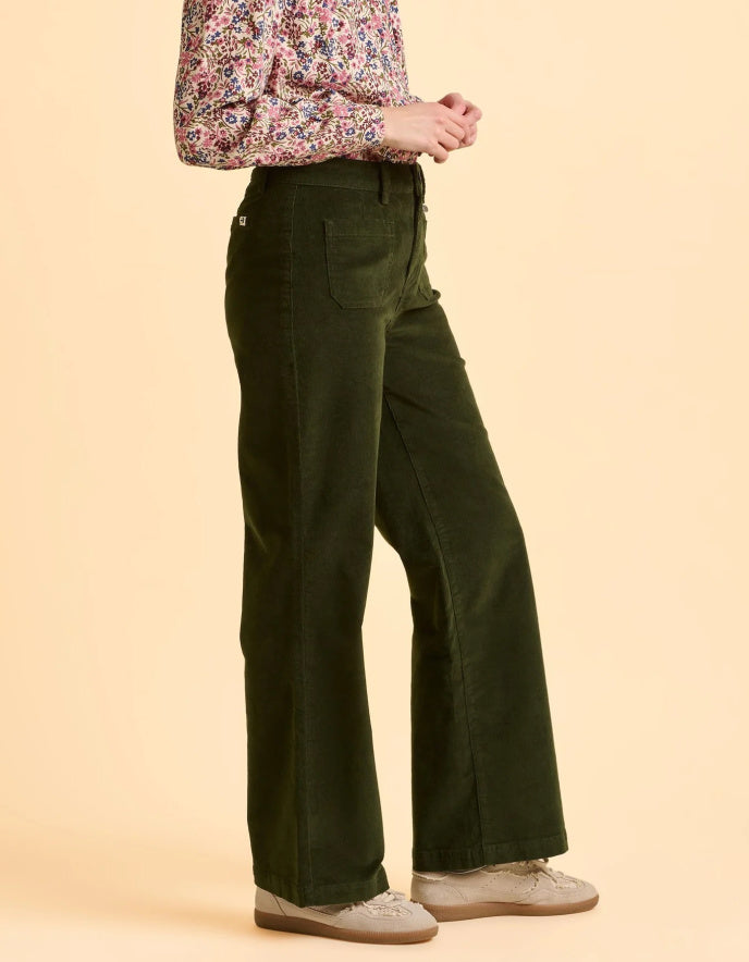 Person wearing green flared pants and a patterned shirt on a beige background