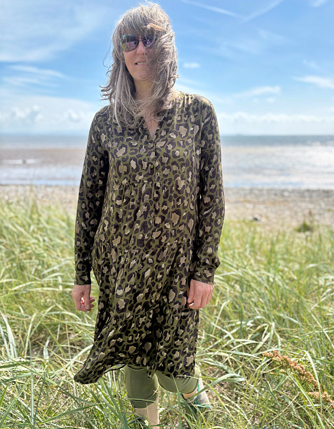Person wearing a leopard print dress standing on a grassy field with a beach and blue sky in the background
